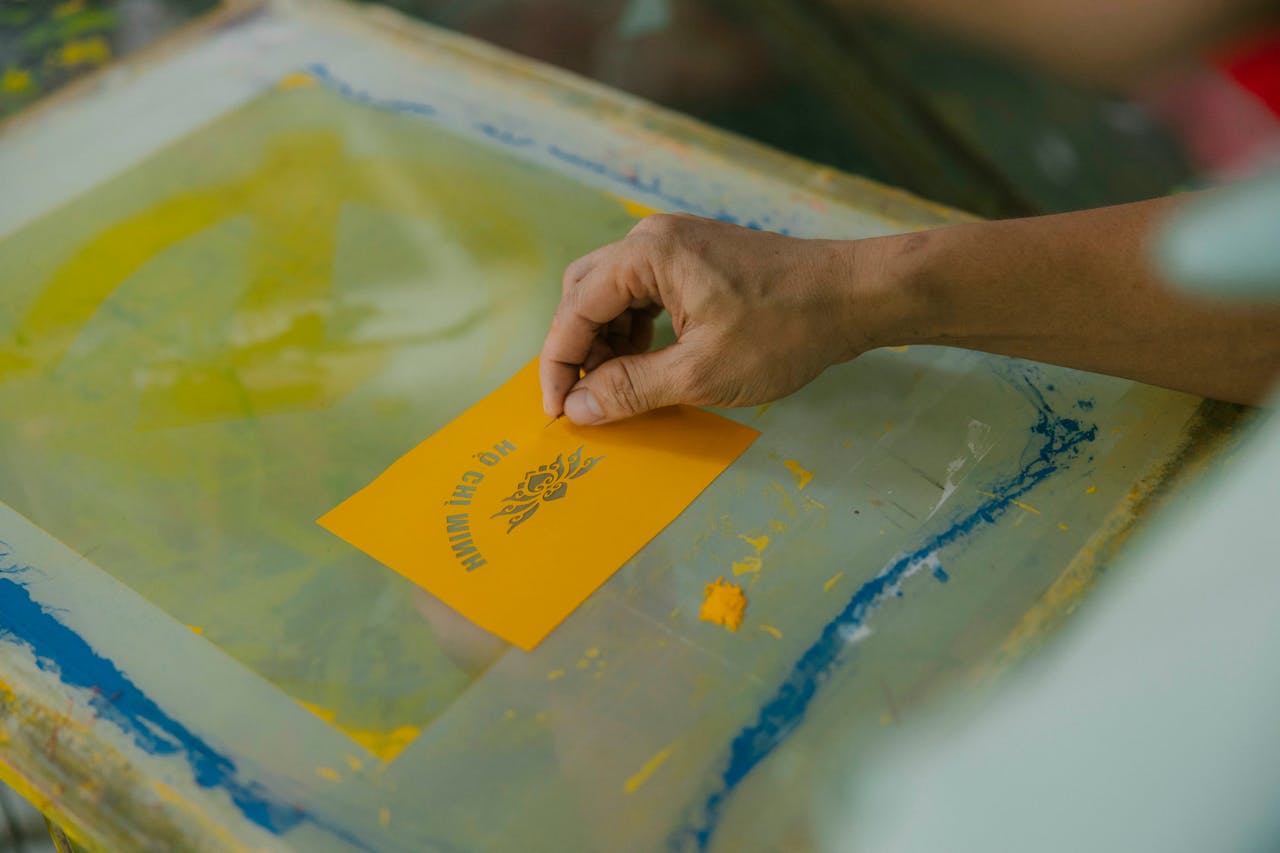 who-we-are A detailed look at a hand screen printing, focusing on a yellow card with design.
